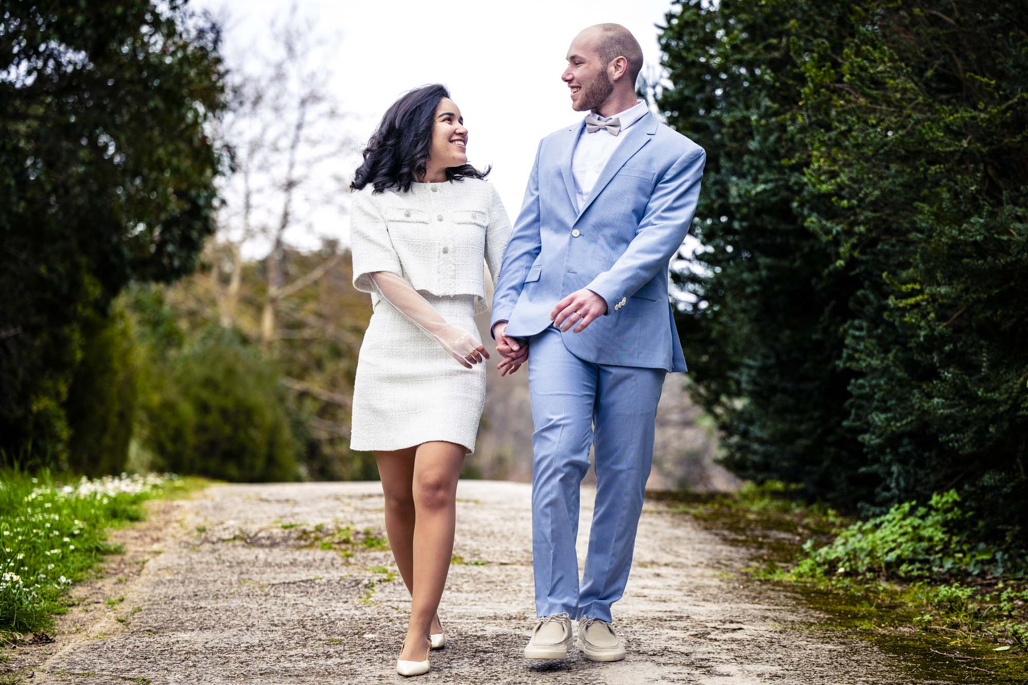 Couple de mariés marchant main dans la main en se regardant avec complicité dans un parc à Marseille - Photographe Mariage Provence.